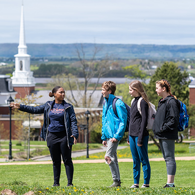A student gestures as she leads a group of prospective students on a campus tour. The chapel is visible in the background.